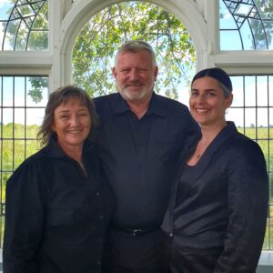 The image shows the Rosebrooke core team standing in front of the Bell Tower window. From left to right is Alice Capper-Starr, Evan Williams and Monika Nichols.