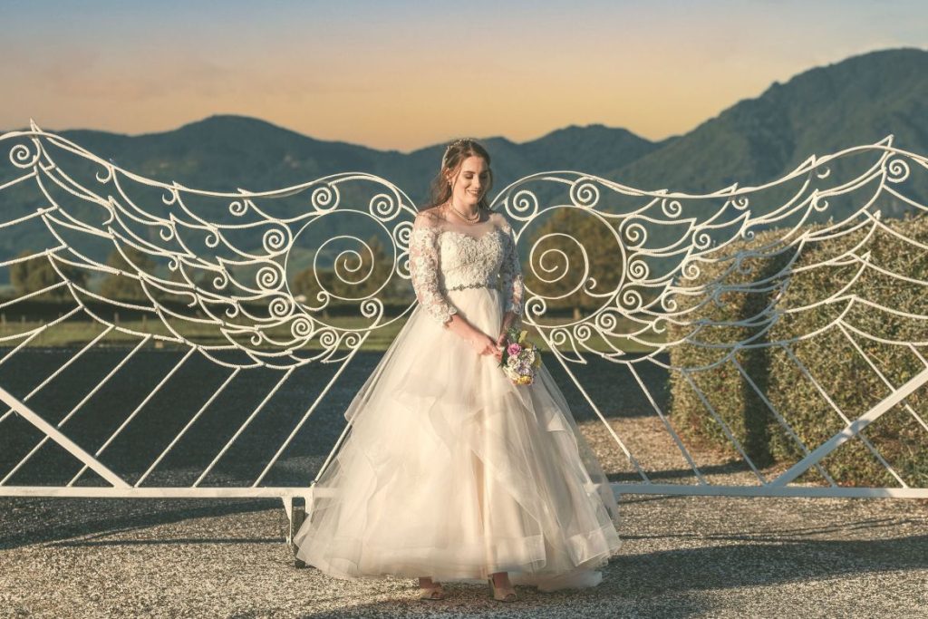 A bride stands in front of the white angel wing gates