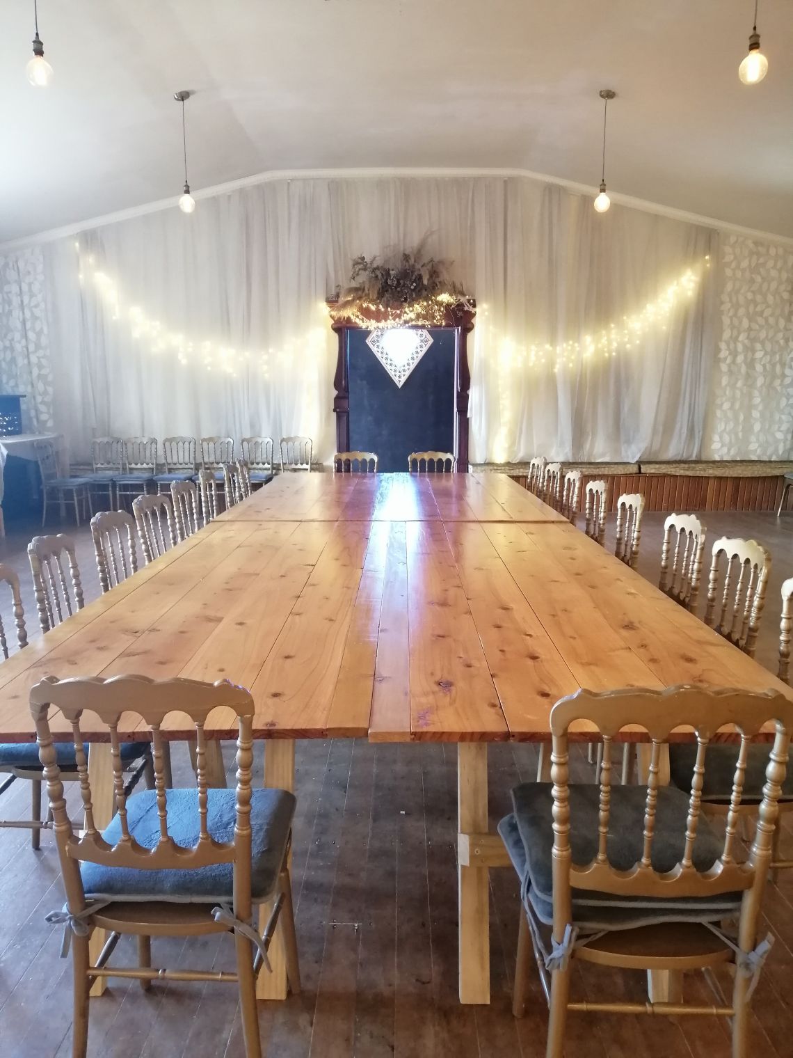 A large table surrounded by gold chairs with fairy lights ont he wall in the background.