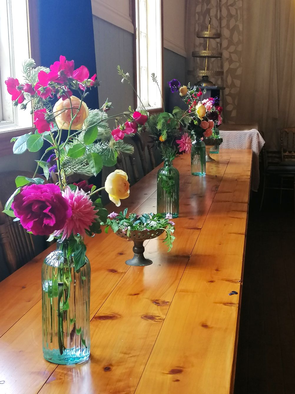 Bright colourful flowers in brass vases placed along a table.
